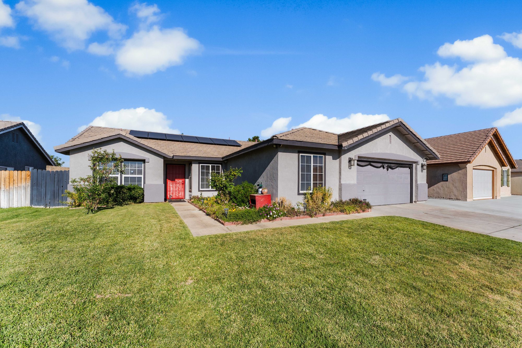 A single-story stucco home with a red front door and a green lawn